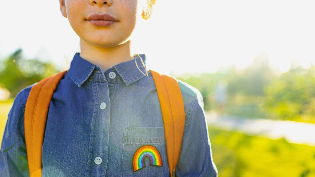 child wearing denim shirt with rainbow patch and orange backpack