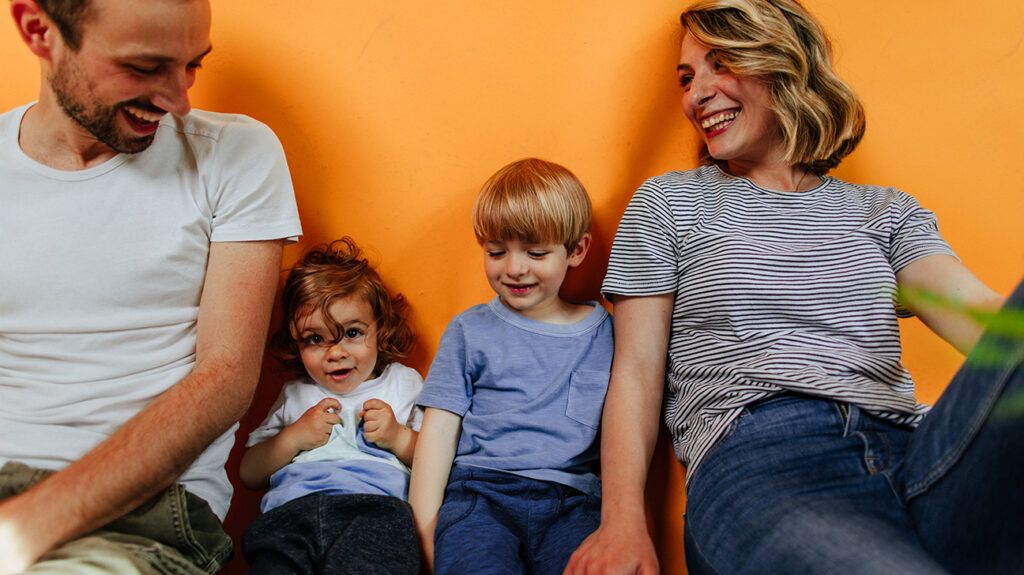 Family sitting against orange wall smiling 