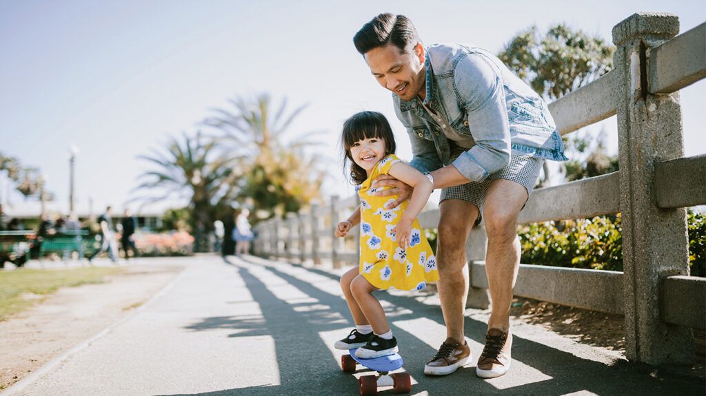 Father helping daughter ride skateboard