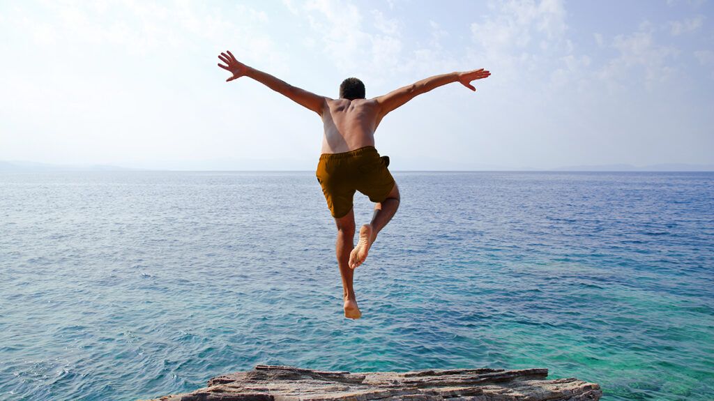 man diving off cliff into the ocean