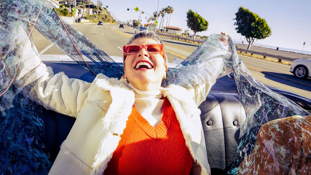 Woman laughing in a convertible with arms overhead