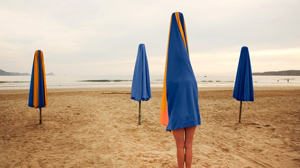Person covering up under a beach umbrella for feelings of body shame