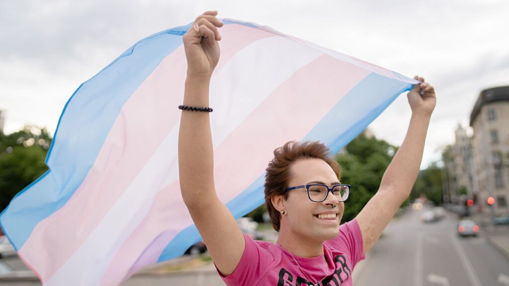 Person holding a transgender Pride flag over their head in celebration