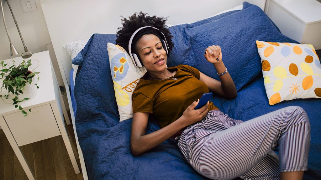 Woman with headphones lying on her bed looking at her smartphone