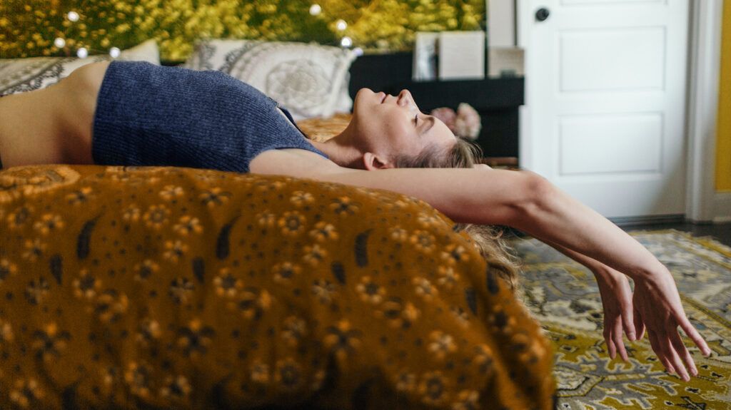 A woman lying in bed with her eyes closed and arms stretched overhead