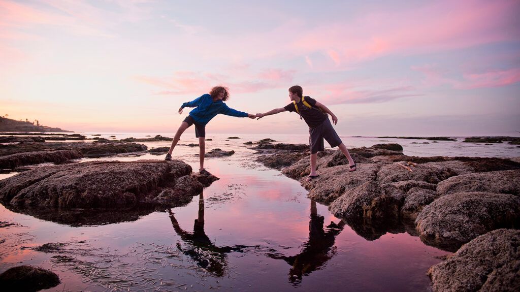 Kids helping each other across tidal pool during sunset