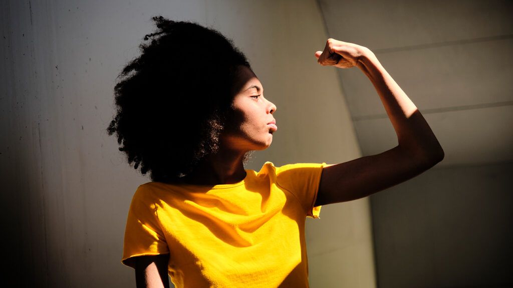 young woman in a yellow shirt flexing arm muscle 