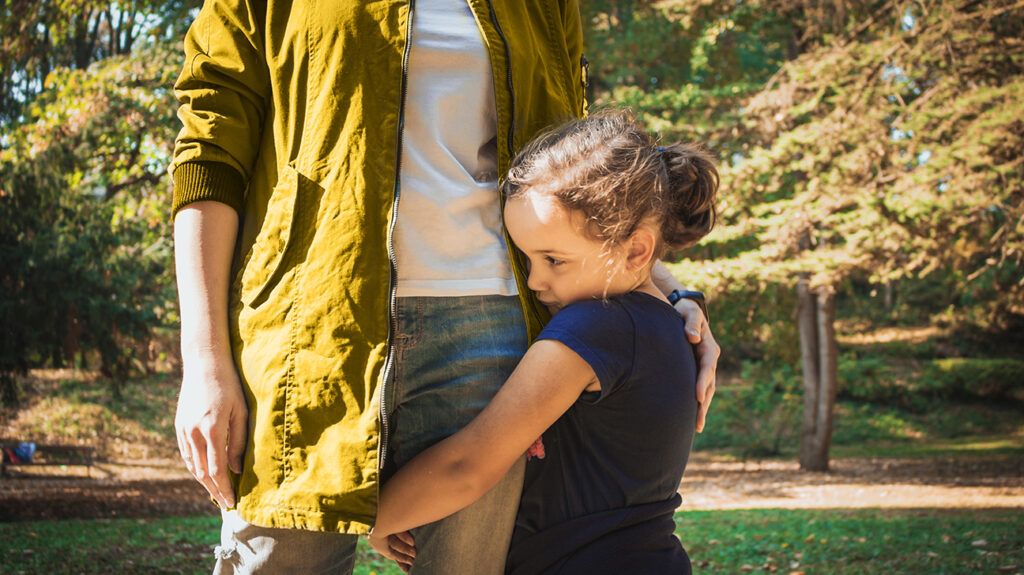 little girl clinging to the inner thigh of her mom, looking away from the stranger whom she is anxious about