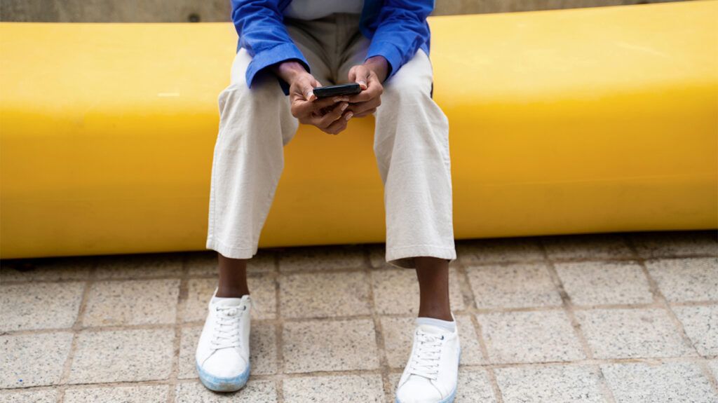 Man with white shoes sitting and looking at phone