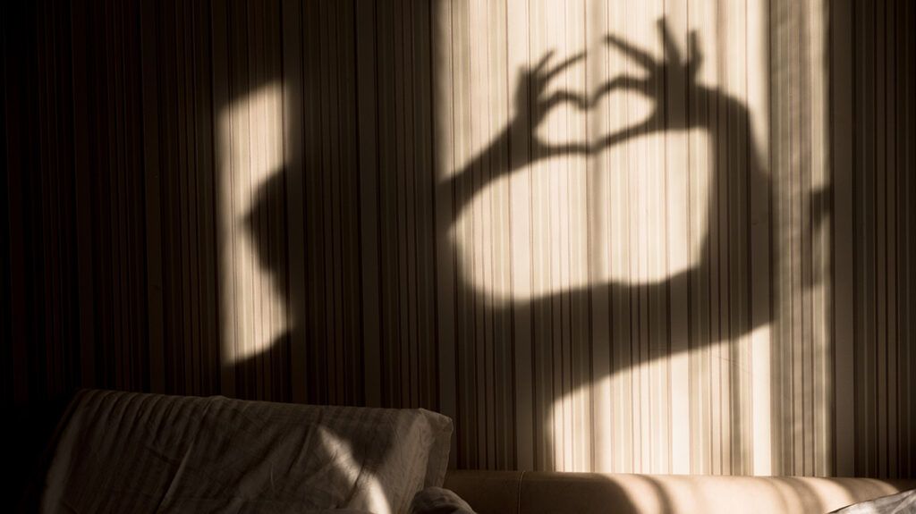 Person making heart shadow with hands on wall
