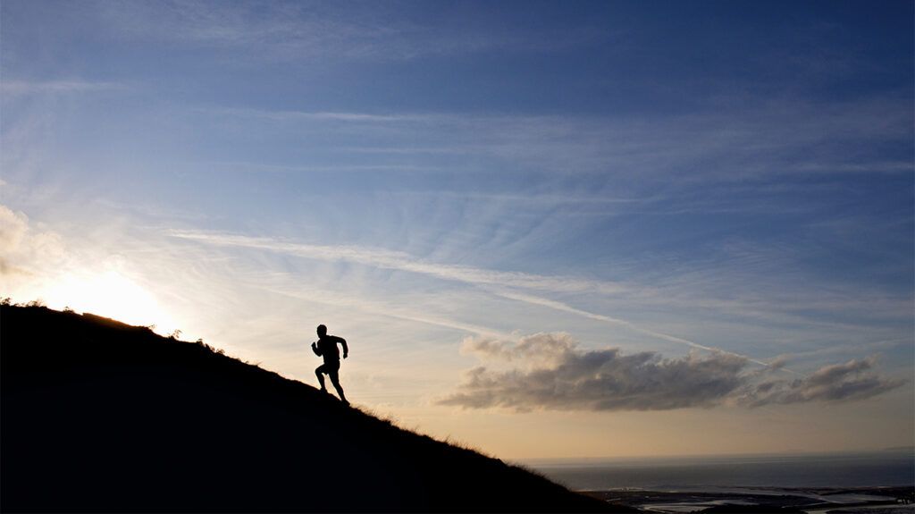 The silhouette of a person climbing a mountain against an open sky