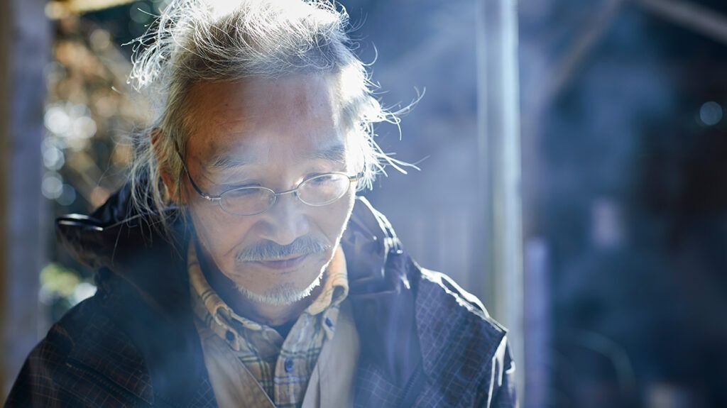 An older Asian man wearing glasses and looking sad