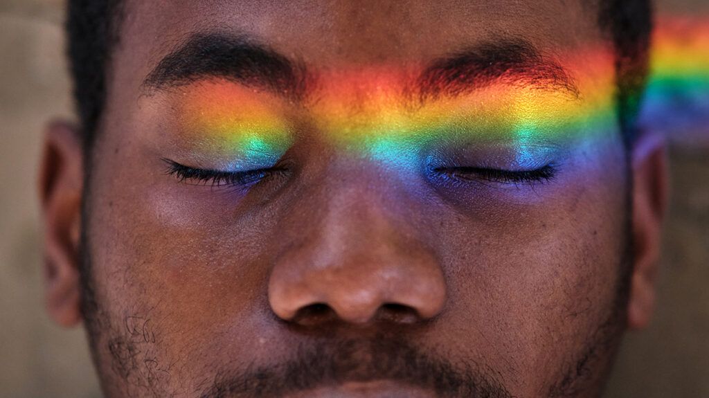 close up of a man with his eyes closed and rainbow light across his eyes