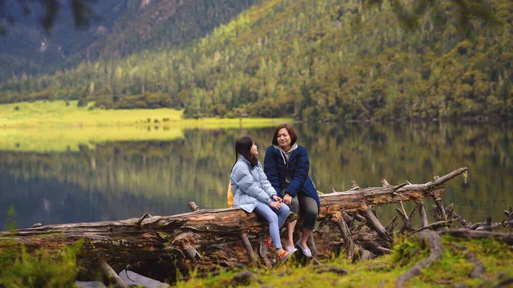 a mom and daughter sitting on a fallen tree in nature