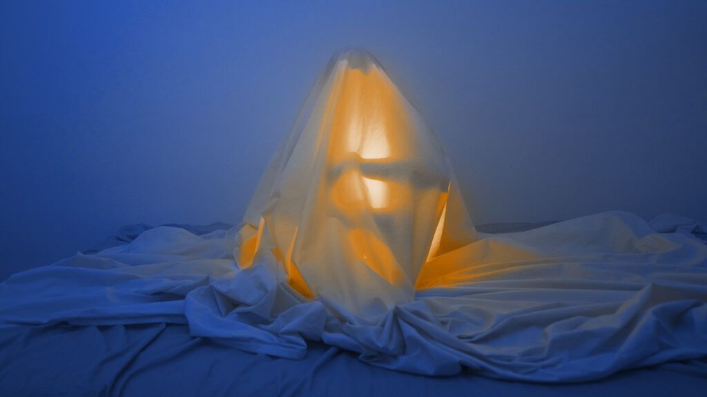 a person under bed sheets with a glowing light turned on