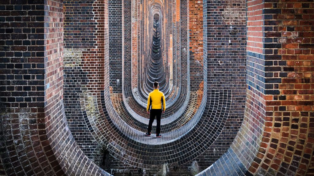 Man standing on bridge looking at architecture in a seeming echo of itself, symbolic of existential theory