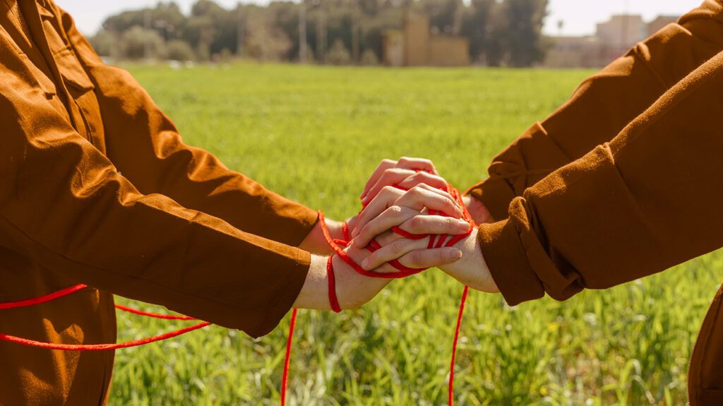 Codependent couple with red yarn tangled on their clasped hands