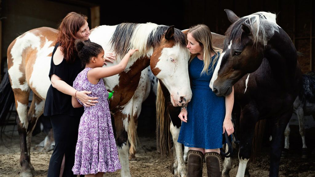 Young girl participating in equine assisted therapy alongside therapist, trainer, and horse