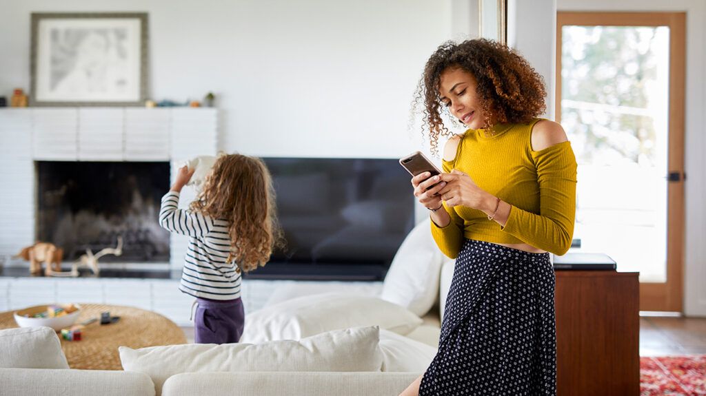 a mom using her phone while her daughter plays in the living room
