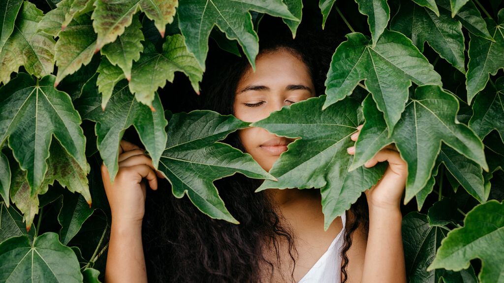 a woman standing behind large leaves with her eyes closed