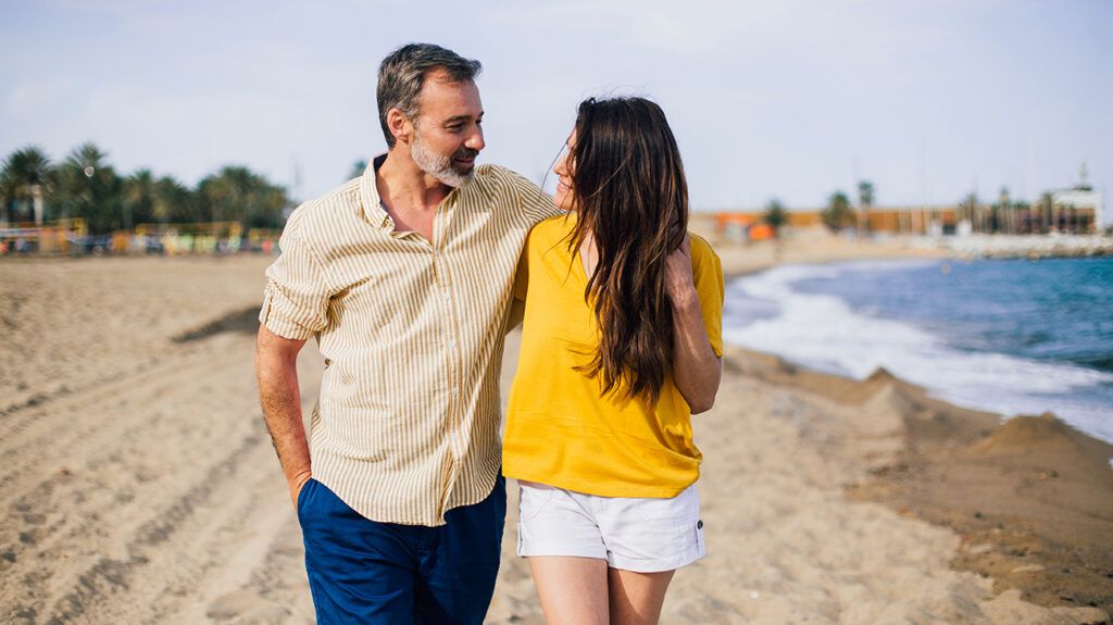 Older man and younger woman walking on the beach