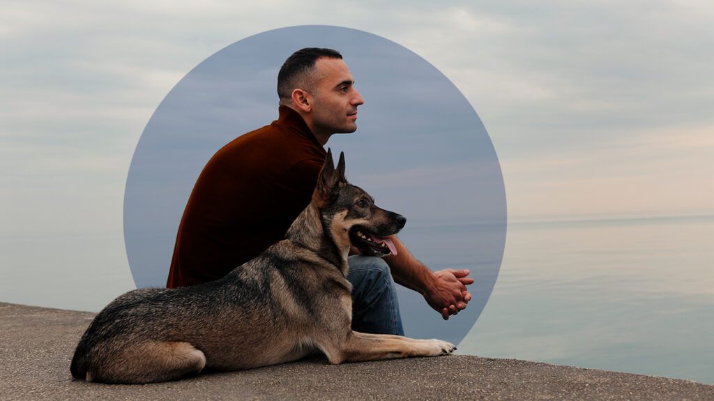 a man sitting with his dog while looking at the lake