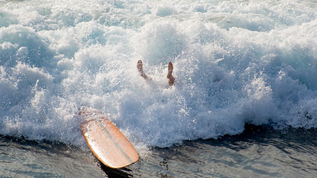 someone's feet in the air above the foam in the crash of wave near surfboard, symbolic of failing