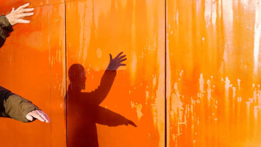 Man doing tai chi and watching his shadow on a sunkissed orange wall