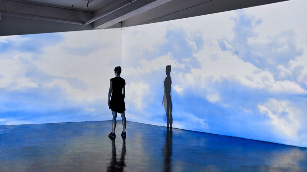 a woman standing in front of a projection wall with clouds on it