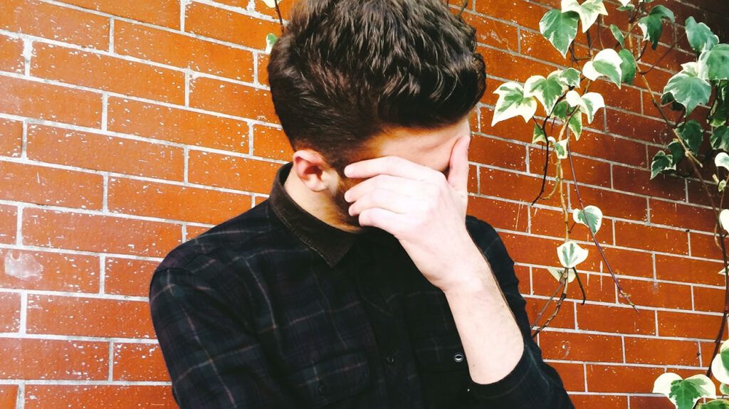 Man covering face with hand embarrassed by his perpetual embarrassment