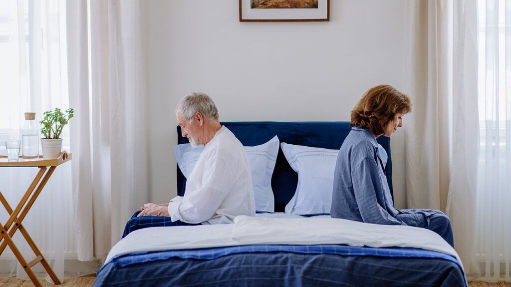 Couple sitting on opposites sides of bed, one lonely in their marriage