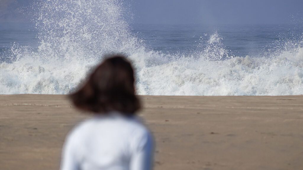 Woman gazing at crashing waves, symbolism of her breakup grief not lost on her