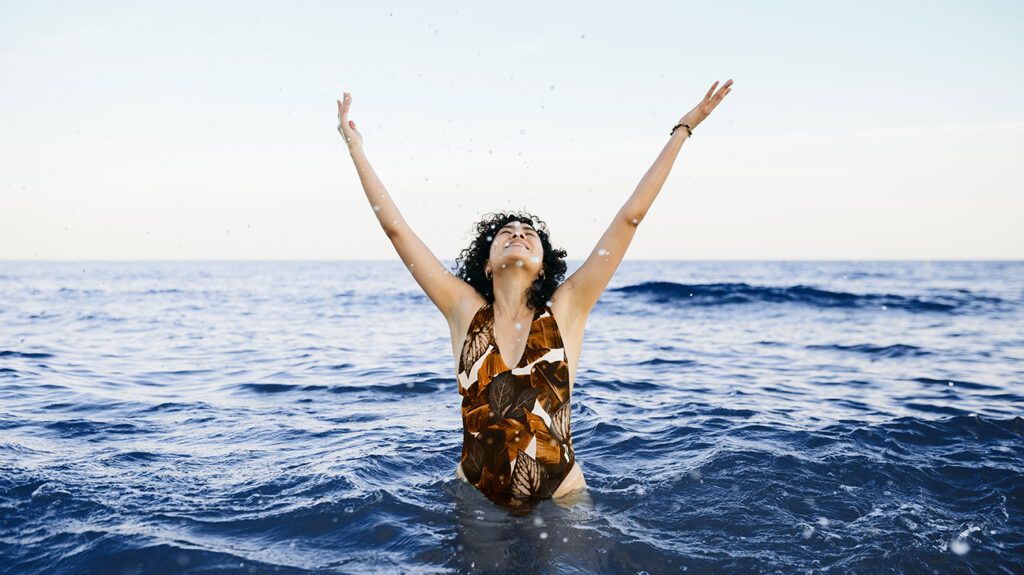 a woman standing in the ocean splashing water above her head