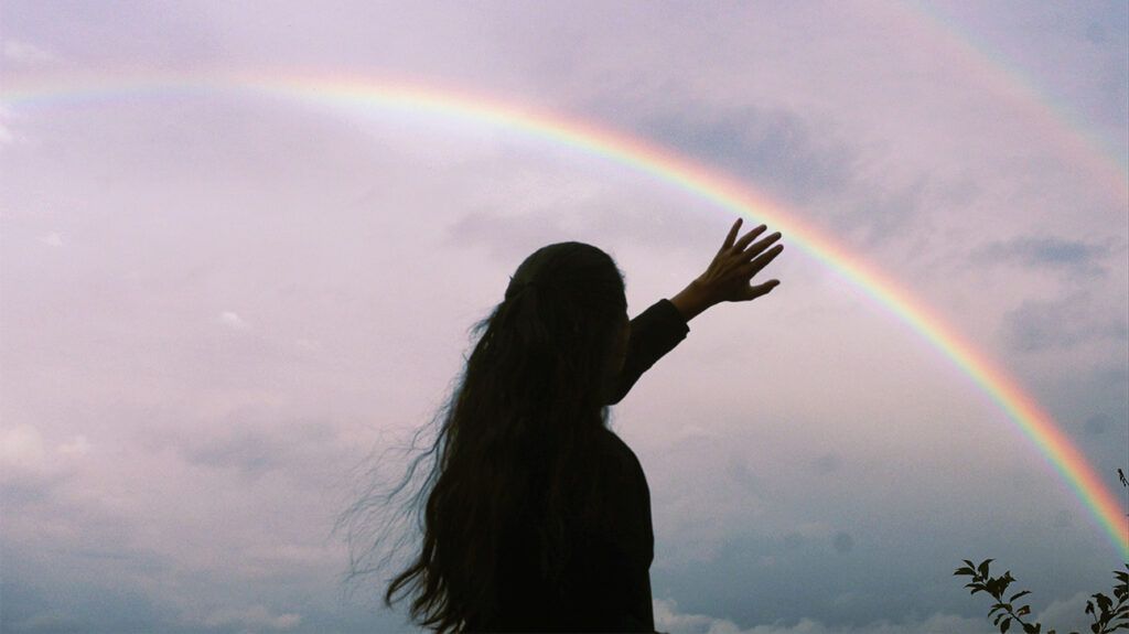 a person reaching for a rainbow in the sky