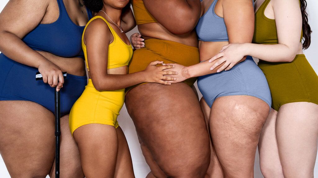 women with different body types in swimwear holding one another