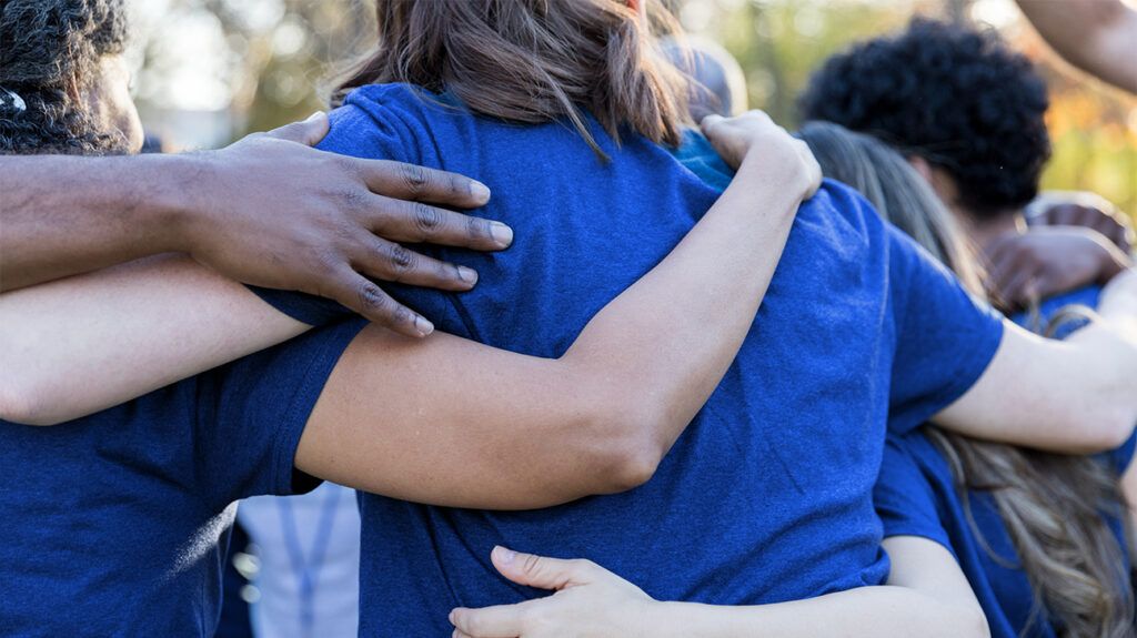 group of people in matching blue T-shirts put their arms around one another's shoulders and waists to show solidarity and support