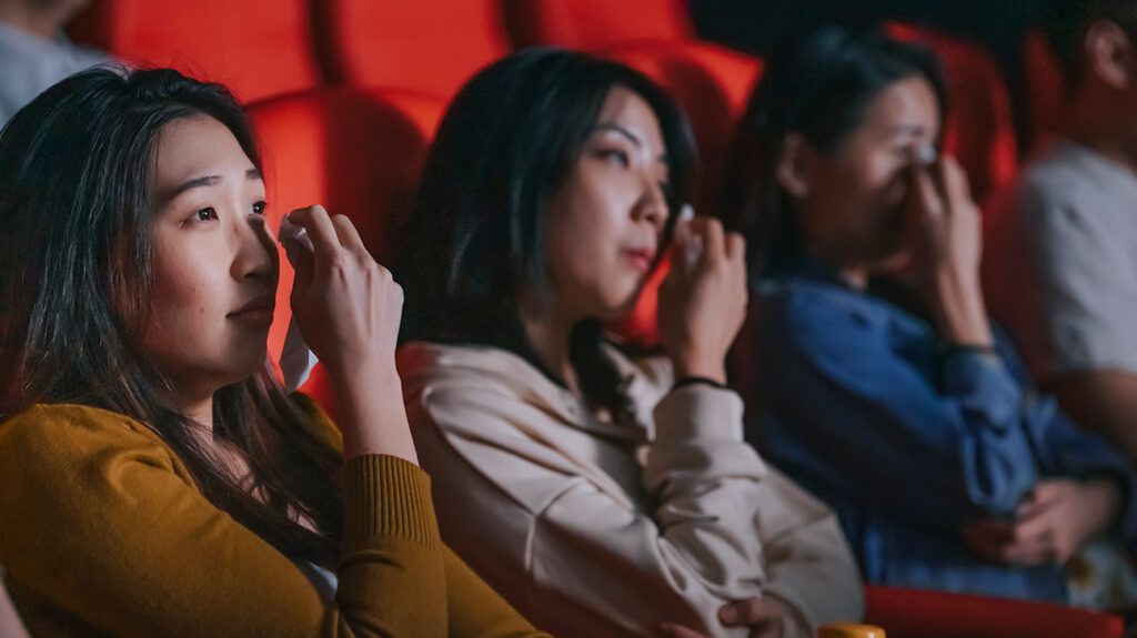 women wiping tears from their eyes in a movie theater 