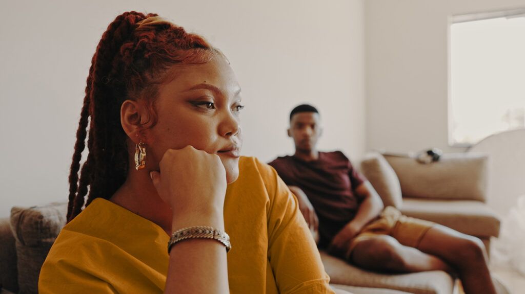 an upset woman ignoring her boyfriend while sitting on the couch with him