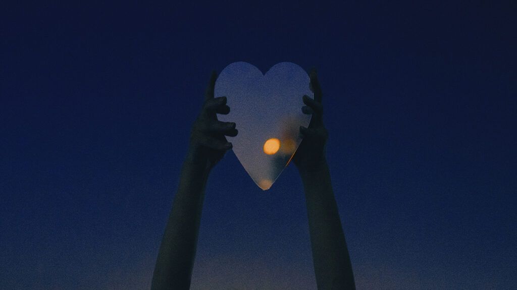 a person holding a heart shaped mirror toward the moon