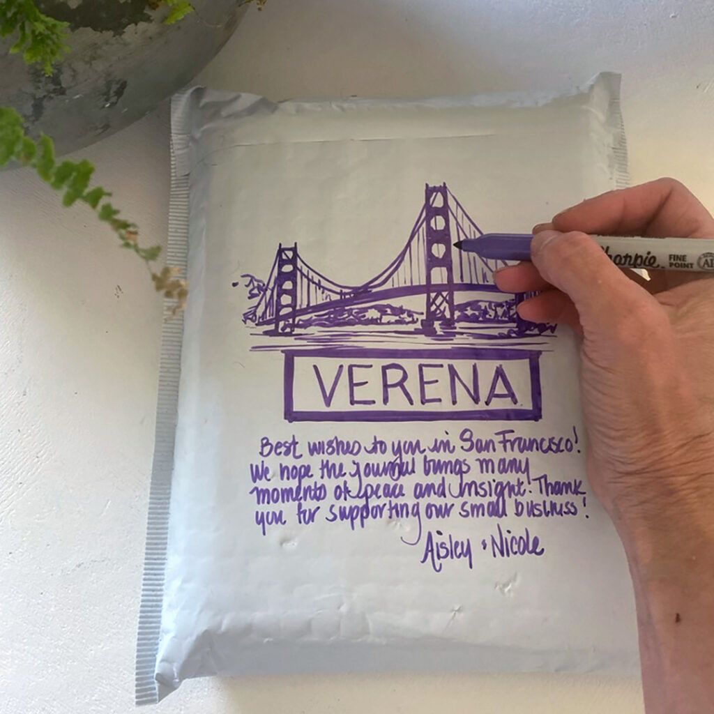 A hand holding a purple sharpie, drawing on a parcel