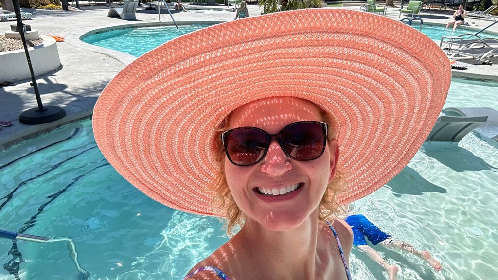 a woman smiling wearing a wide brimmed pink hat