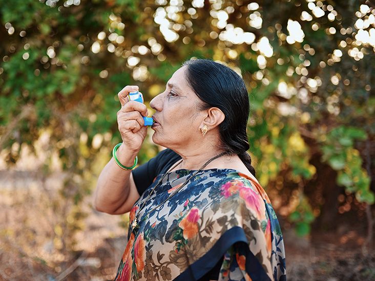 Older adult standing in the outdoors taking a puff from an asthma inhaler as part of their asthma medications treatment plan