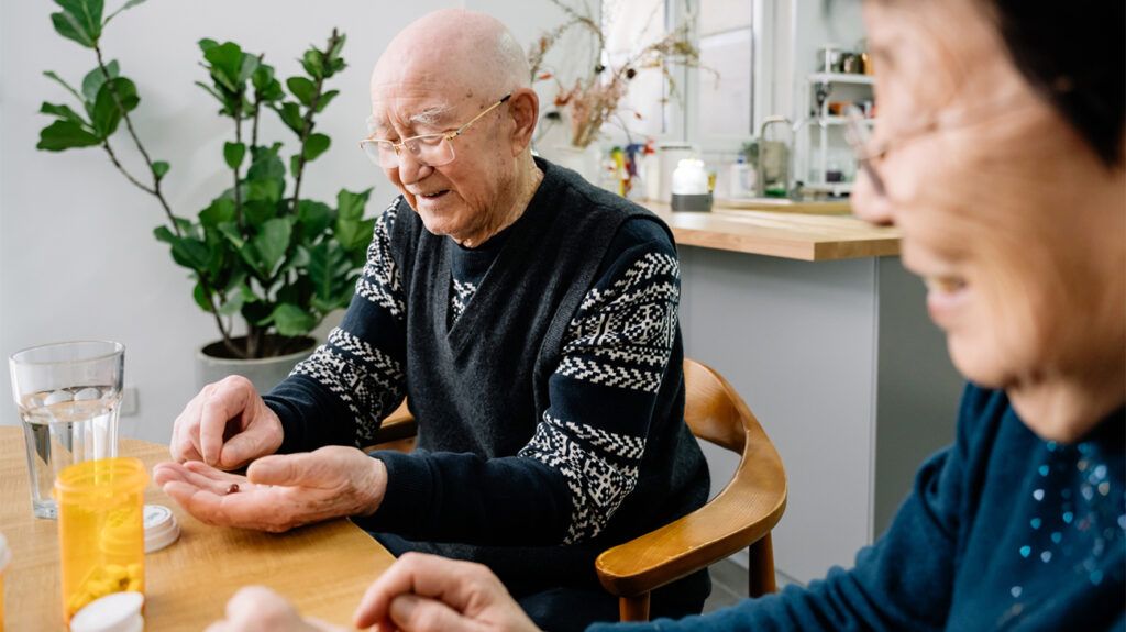 Older adult couple sitting together at a dining table, focus on older adult male as they learn about LDL cholesterol medications