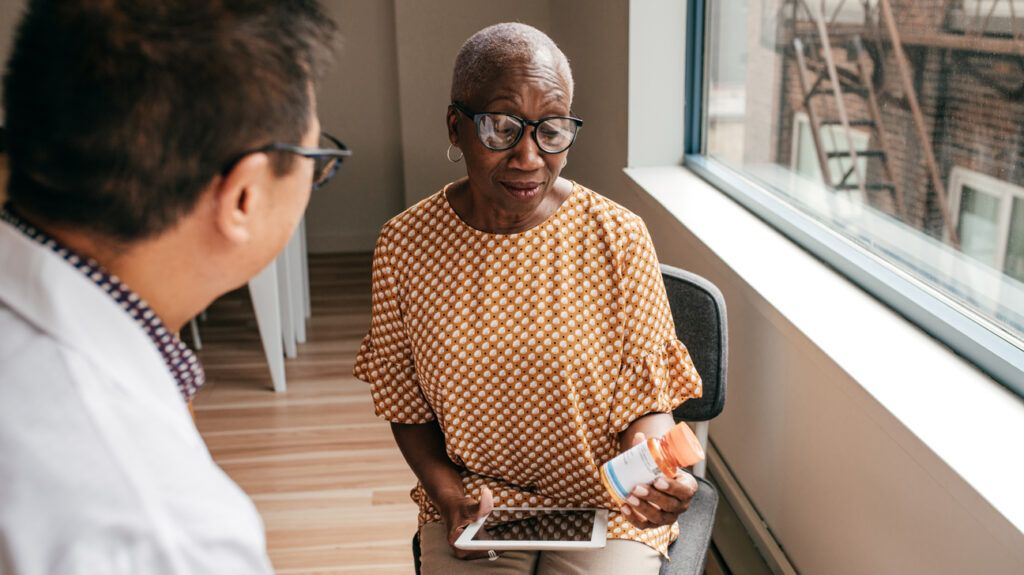 Older female adult reading a prescription pill bottle while talking to a healthcare professional about MS medications