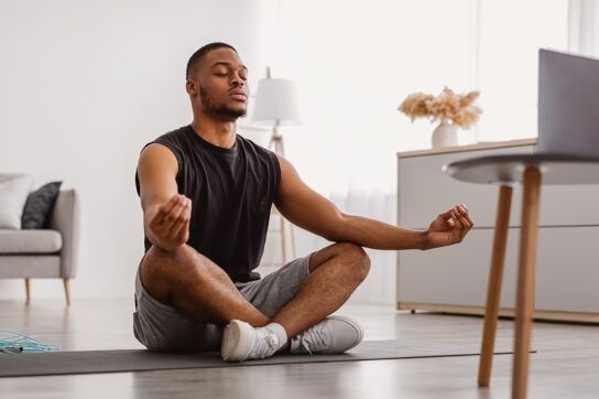 A young adult sitting cross-legged in a mediation pose in front of a laptop, wondering when is the best time to take amlodipine