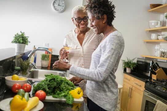 A couple in a kitchen with a lot of vegetables around them, which are good foods for a diverticulitis diet.