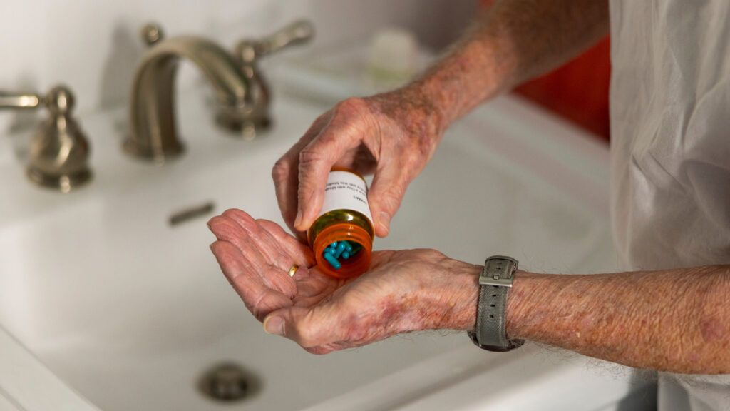 A person dropping a pill from a bottle into their hand