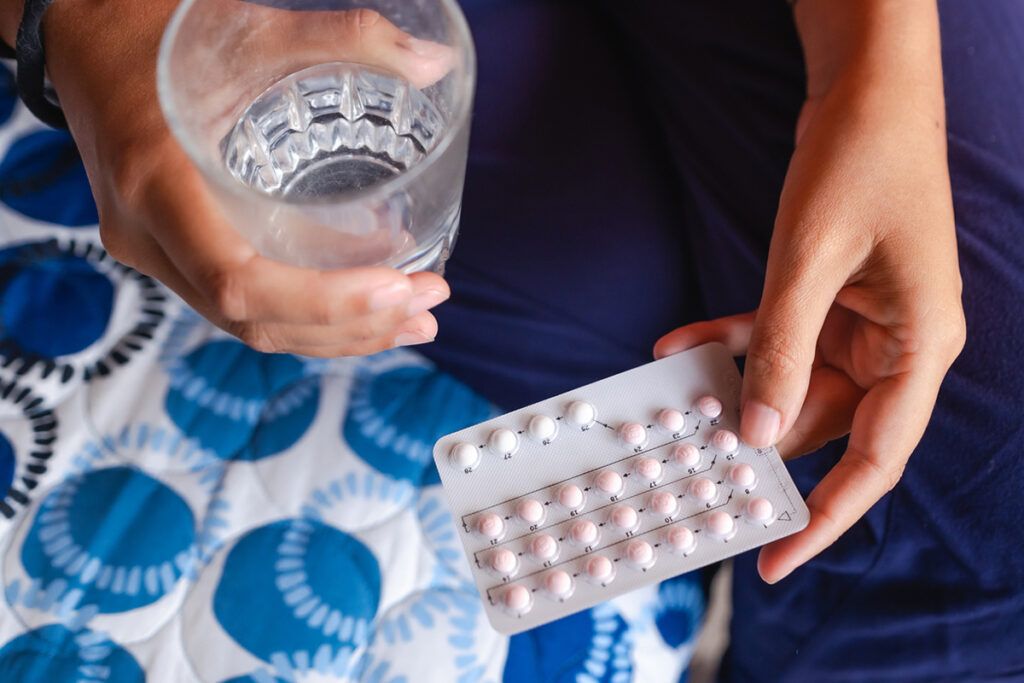 A person holding a glass of water and birth control pills