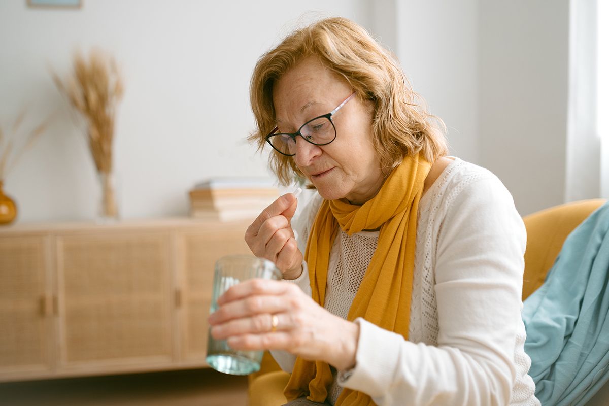 An older woman sitting down taking a prednisone pill, wondering how long it will take to work.