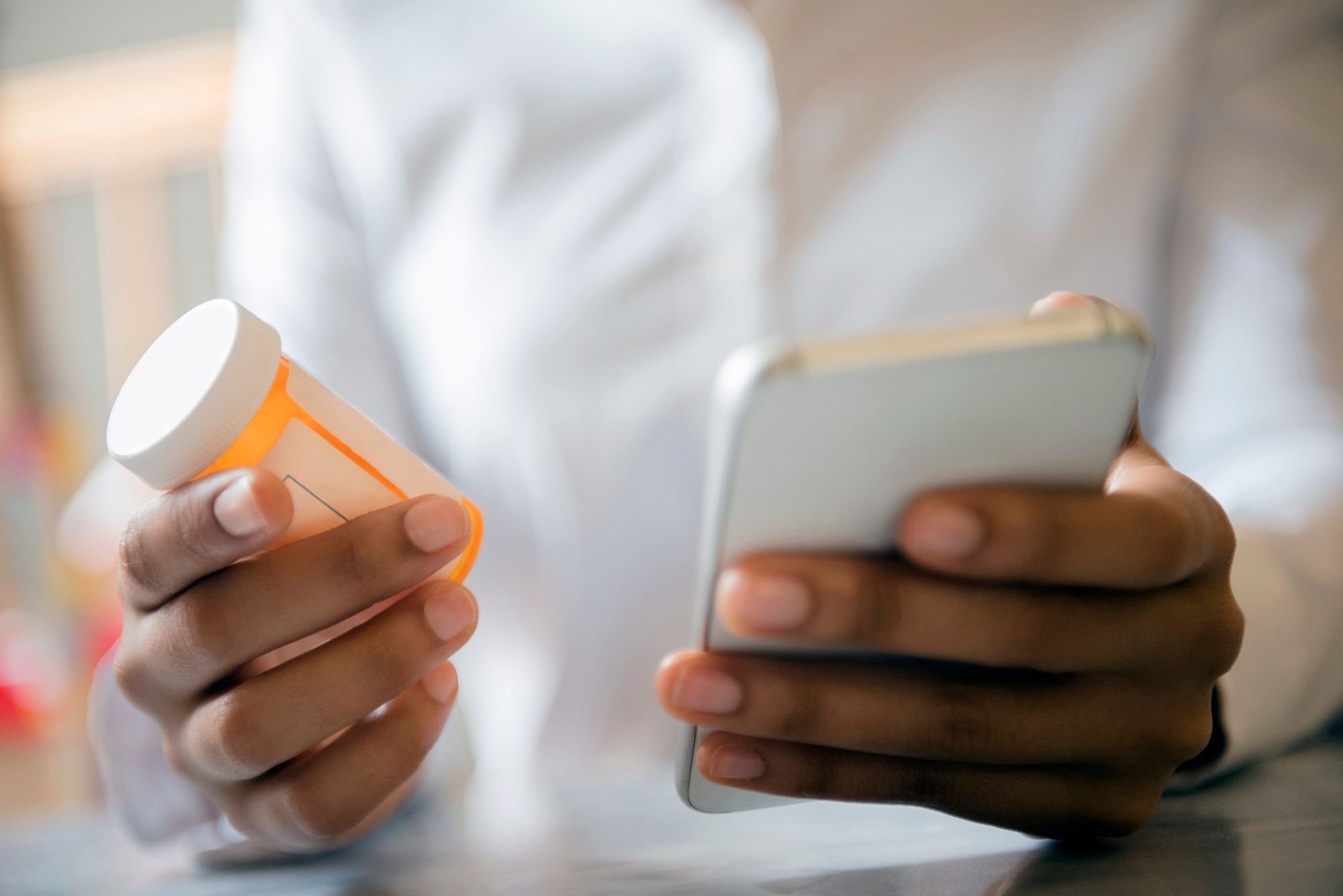 Someone holding a phone and a pill bottle, representing taking both Prozac and Adderall and whether it is safe.